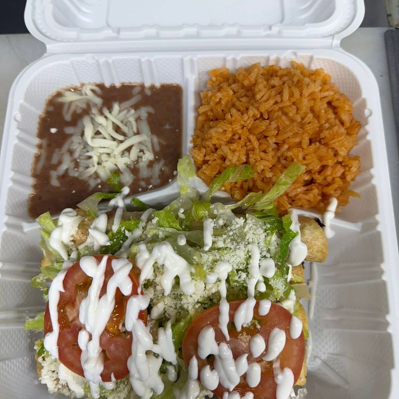 A takeout plate with Mexican rice, refried beans and a dish topped with lettuce, tomato, crema and queso